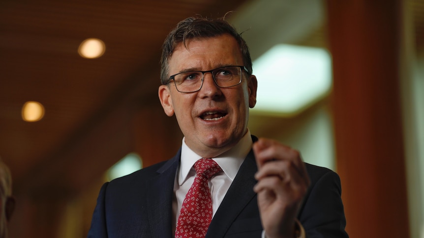 Alan Tudge wearing glasses and a suit and red tie mid-sentence using his hand to emphasise a point