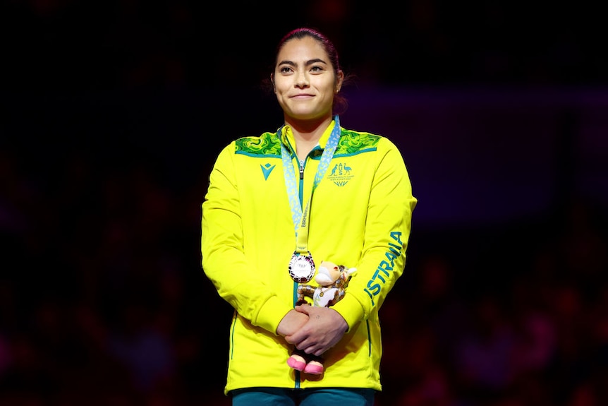 gymnast georgia godwin stands on a podium with a silver medalholding a mascot