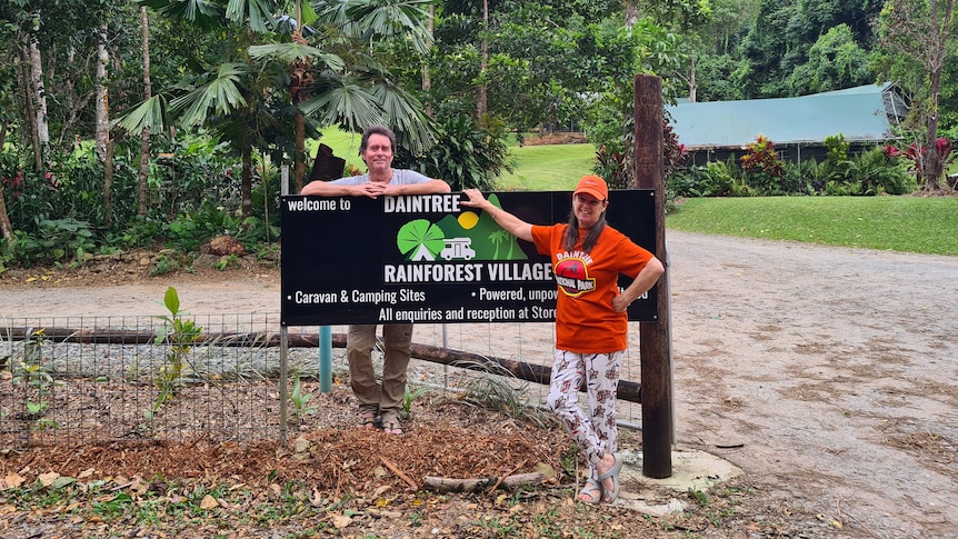 A man and a woman standing next to the entrance sign of their business.