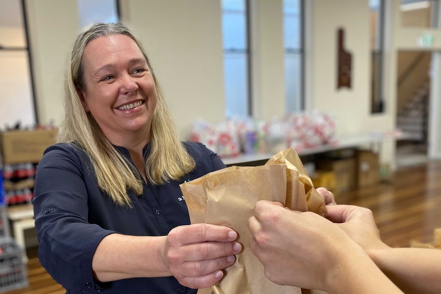 A smiling woman hands out bags of food inside a crisis centre.