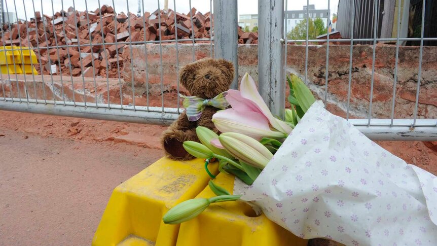 A teddy bear and a bunch of flowers are left at the site of a deadly wall collapse in Carlton