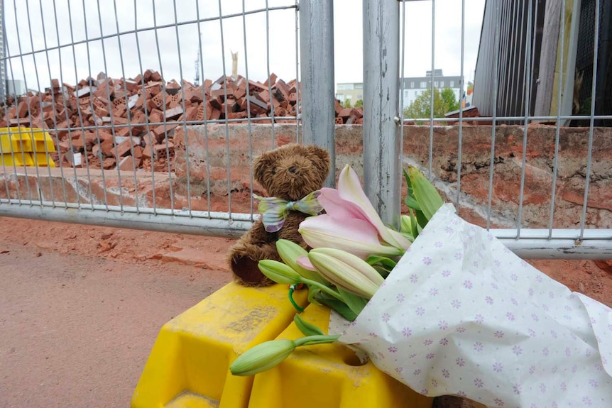 A teddy bear and a bunch of flowers are left at the site of a deadly wall collapse in Carlton