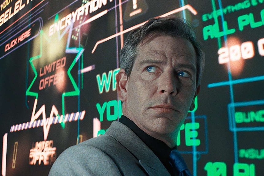 Colour still image from 2018 film Ready Player One Ben of Mendelsohn standing in front of a wall of neon graphics.