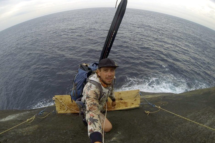 A man standing on a wooden ledge above the ocean