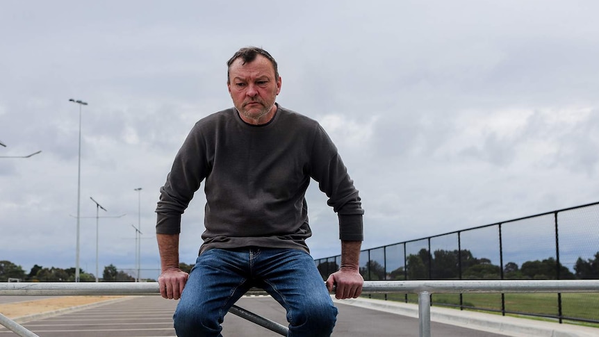 A man sits on a rail overlooking a road.