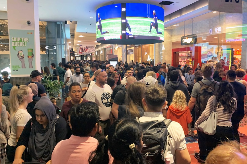 A crowd of people walk through a packed shopping centre.