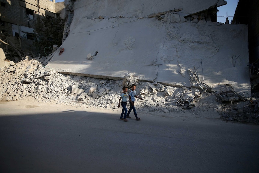 Boys walk near a damaged building on the first day of Eid al-Adha.