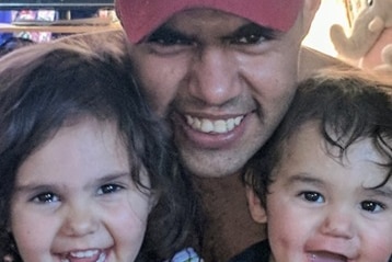 A man in a red cap with his arms around two young children. All three are smiling.