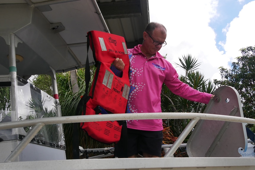 A middle aged man wearing a long sleeve pink shirt putting life jacket into a tub on a boat. 