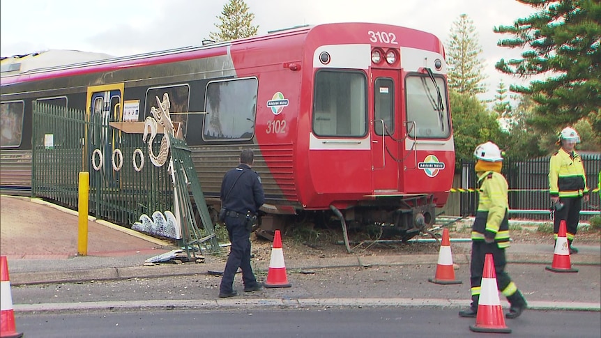 Three people stand around a red train, next to it is a damaged fence