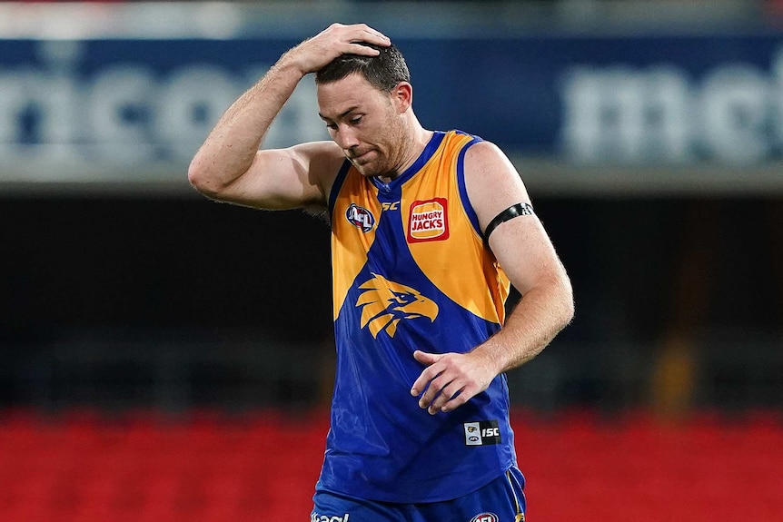 A dejected West Coast Eagles defender Jeremy McGovern looks down with his hand on his head.