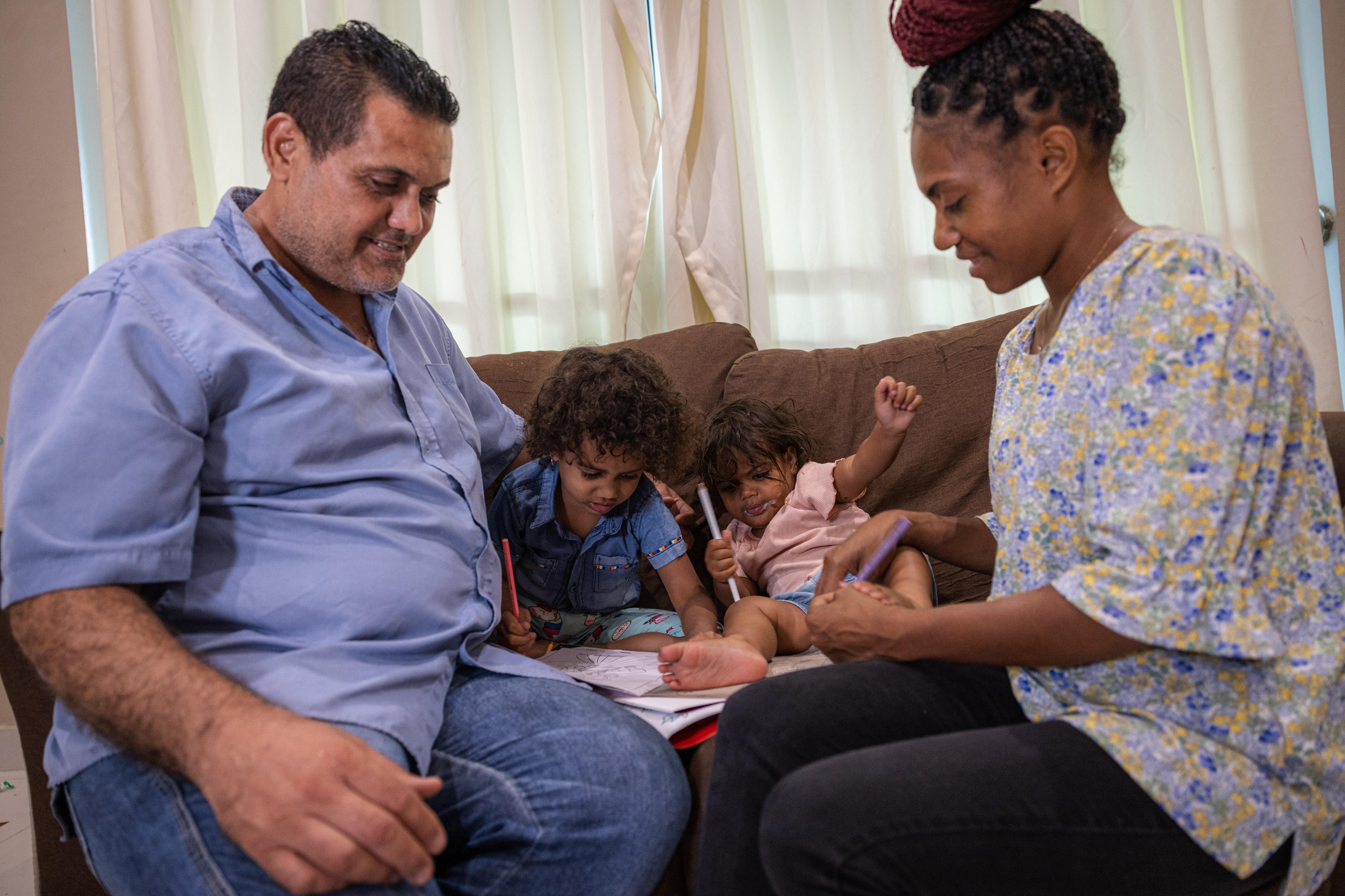 Four family members sit on the couch, the children are colouring in 