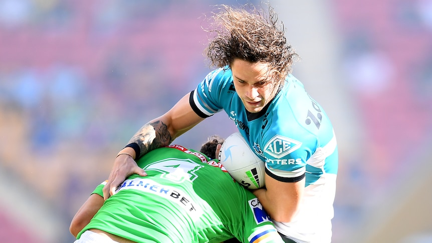 A Cronulla Sharks NRL player holds the ball while being tackled by a Canberra Raiders opponent.