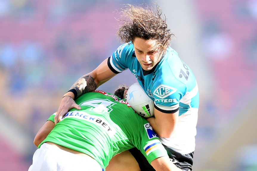 A Cronulla Sharks NRL player holds the ball while being tackled by a Canberra Raiders opponent.
