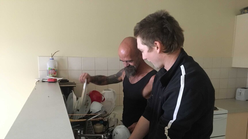 Two men in a kitchen washing dishes.