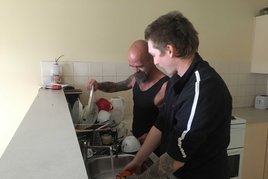 Two men in a kitchen washing dishes.