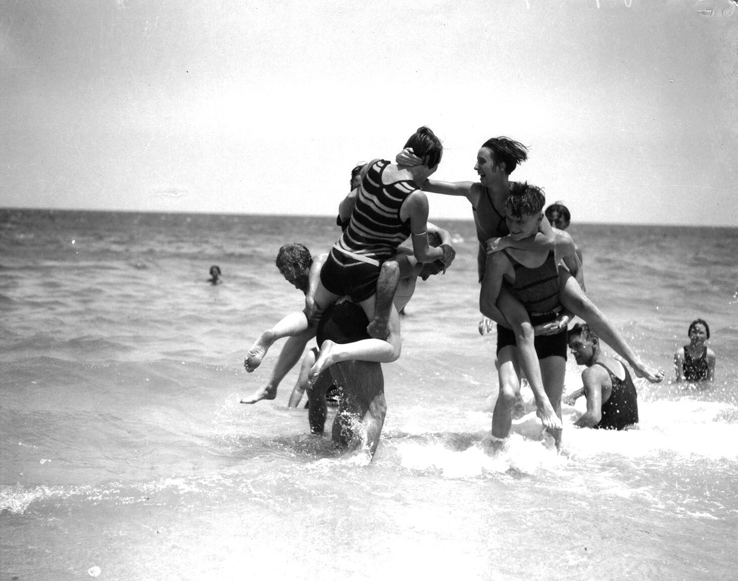 Black and white image of young men at the beach play fighting.