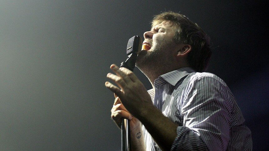James Murphy of LCD Soundsystem sings passionately into a microphone on stage.