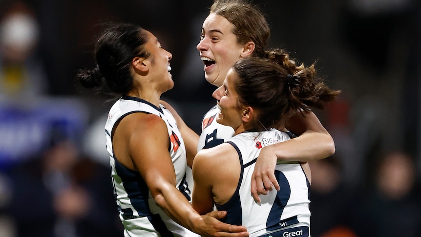 Three Carlton AFLW players embrace as they celebrate a goal against the Western Bulldogs.