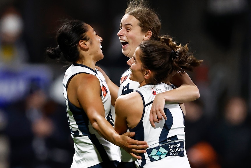 Three Carlton AFLW players embrace as they celebrate a goal against the Western Bulldogs.