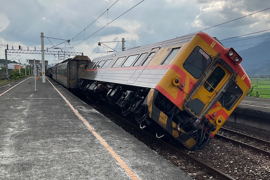 A train car is tilted at a 45 degree angle on the tracks next to the station platform. 