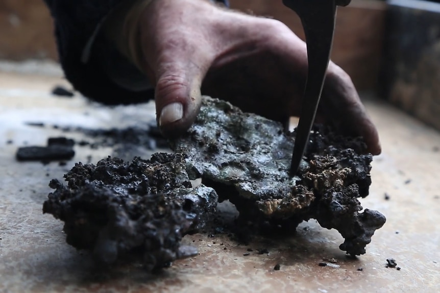 A close up of a blacksmith hammering a hunk of iron made out of boiling placenta blood.