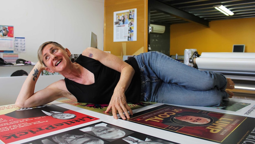 A woman lies on a table that is laminated in satirical magazine covers.