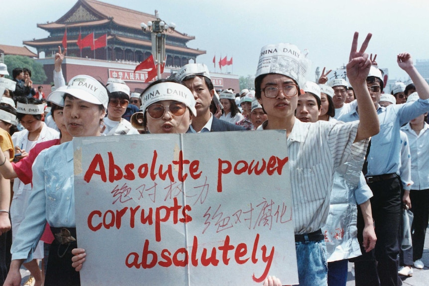 A group of Chinese journalists hold a sign that says "Absolute power corrupts absolutely" and wear hats made out of newspapers.