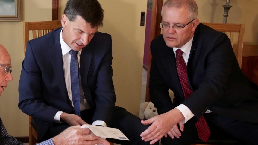 An elderly man holds his electricity bill as Angus Taylor points to it and the Scott Morrison reaches for it