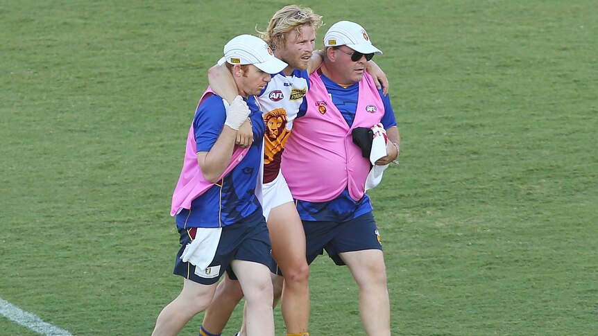 The Lions' Daniel Rich is helped from the field after suffering a knee injury against Gold Coast.