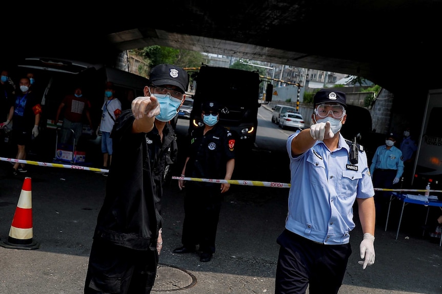 Two policemen in face masks point at the camera