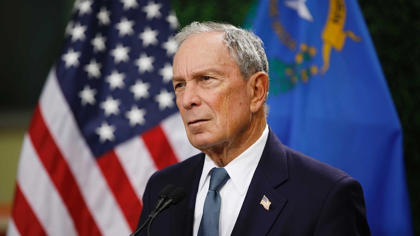 US billionaire Michael Bloomberg stands in front of an American flag.