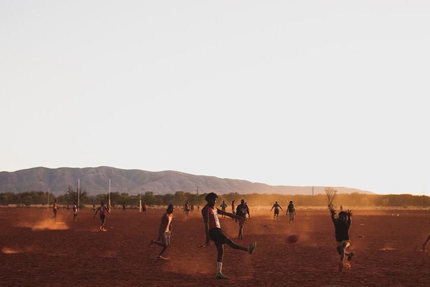 A game of Australia Rules football being played on a desert field in Papunya