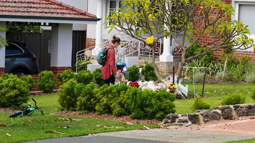 A woman and a young child lay flowers outside a home.