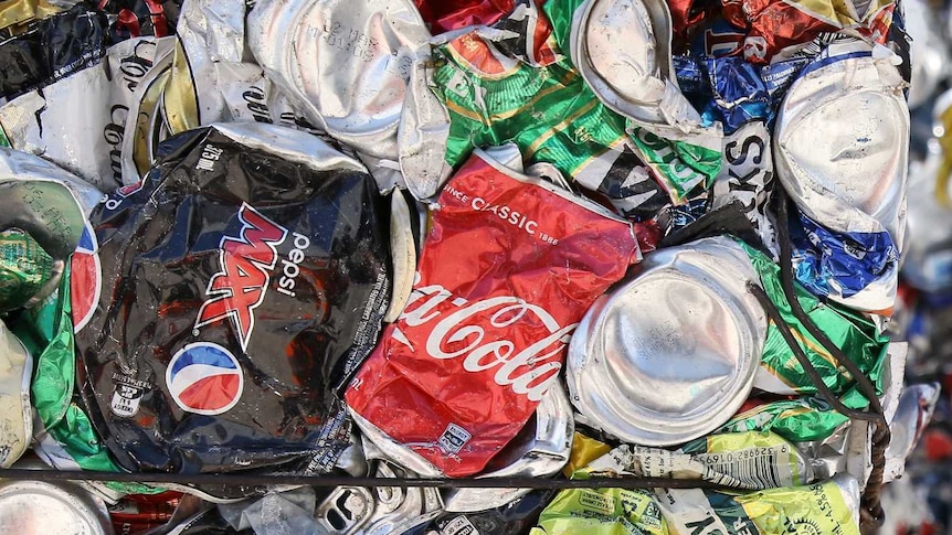 Pepsi, Coke, and alcoholic drink cans are crushed and cubed and stacked next to each other.