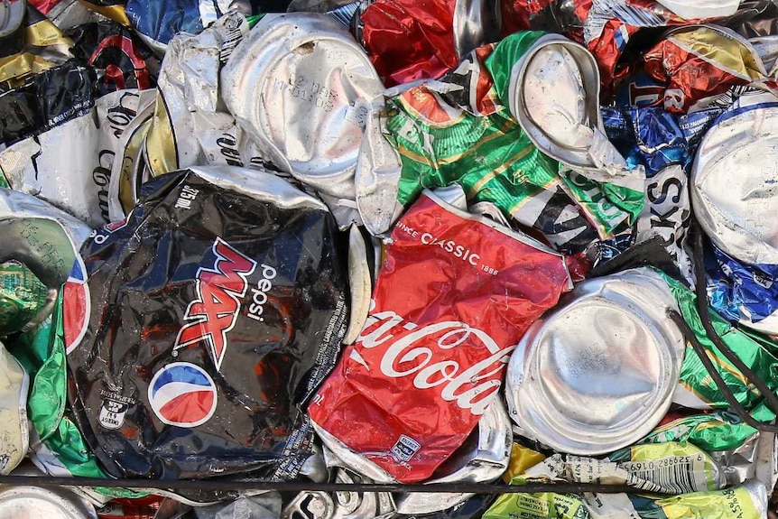 Pepsi, Coke, and alcoholic drink cans are crushed and cubed and stacked next to each other.