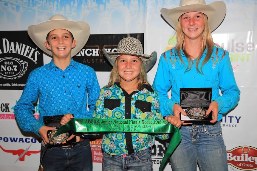 Levi Ward stands next to his sisters Franki and Bobbi.  They all have trophies in their arms. 
