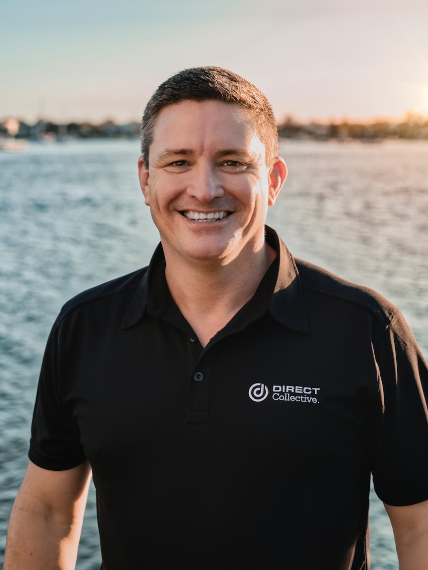 Man in black collared shirt at sunset on the bay smiling at camera