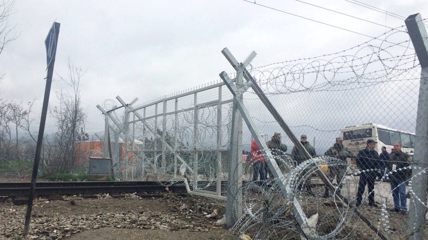 Razor wire covers a fence at the Greece-Macedonia border, with guards standing on the other side of the fence.