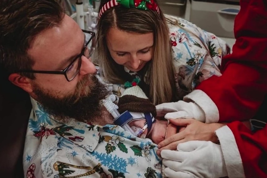 Nathan and Sophie Streeter wear Christmassy clothes in a hospital with Charlie laying on Nathan's chest.