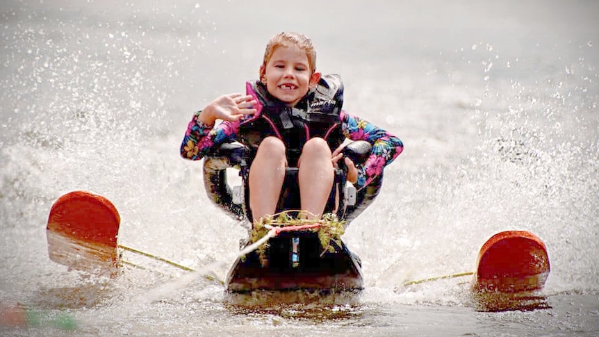 A little girl sits on a special water ski out on the water