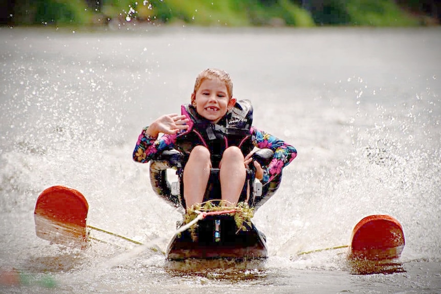 A little girl sits on a special water ski out on the water