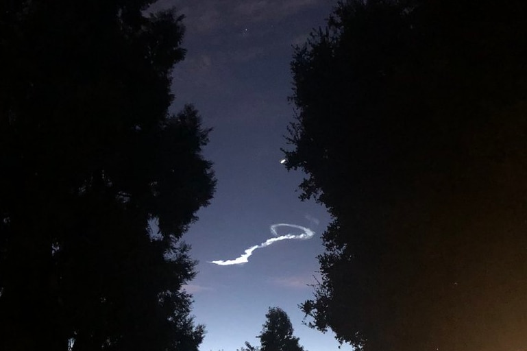 A cloud shaped like a question mark in the sky at dusk, framed by trees