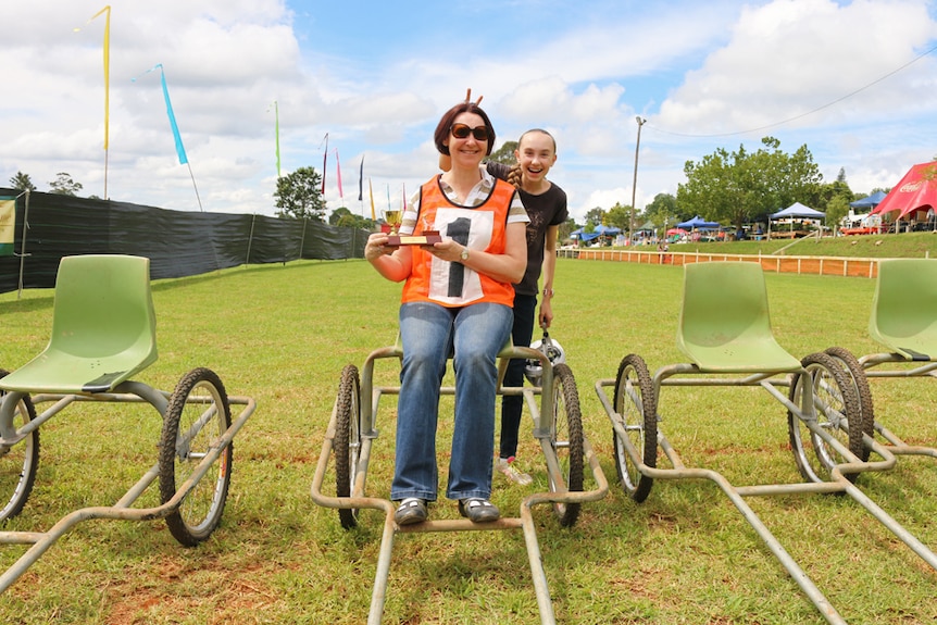 Kerri Fisher sitting on a goat cart with her Comboyne Mountain Goat Races trophy.