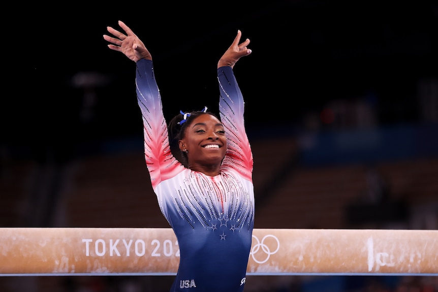 Woman smiling after nailing her balance beam routine at the Olympics.