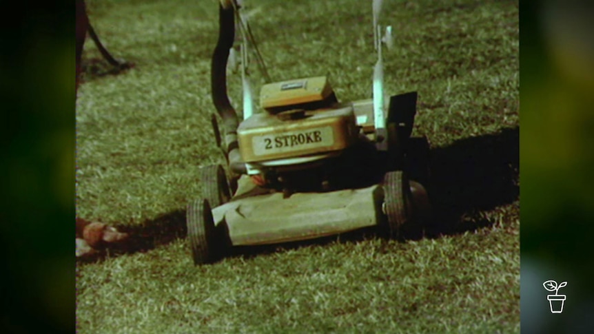 Old photo showing vintage petrol lawn mower with '2 stroke' written on the front