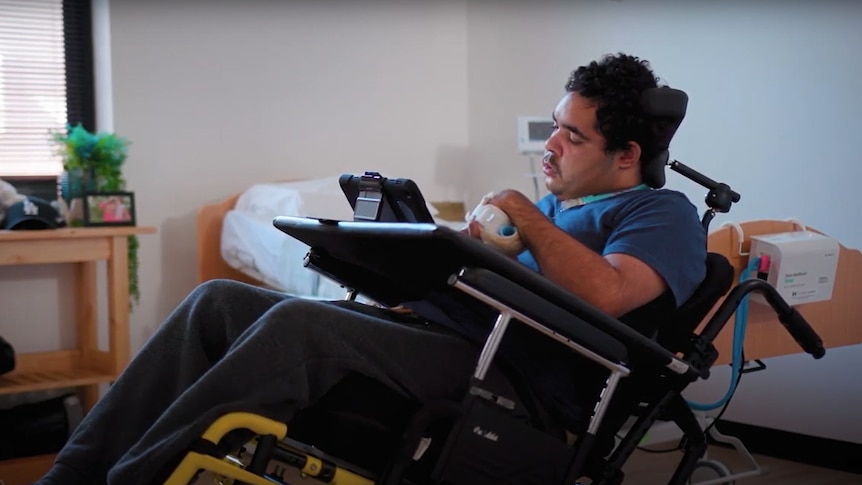 A young man in a wheelchair looking at an iPad. 