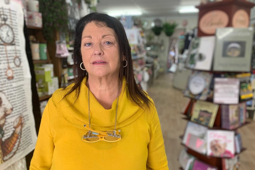 A middle-aged woman in a yellow jumper looks downcast in a gift shop