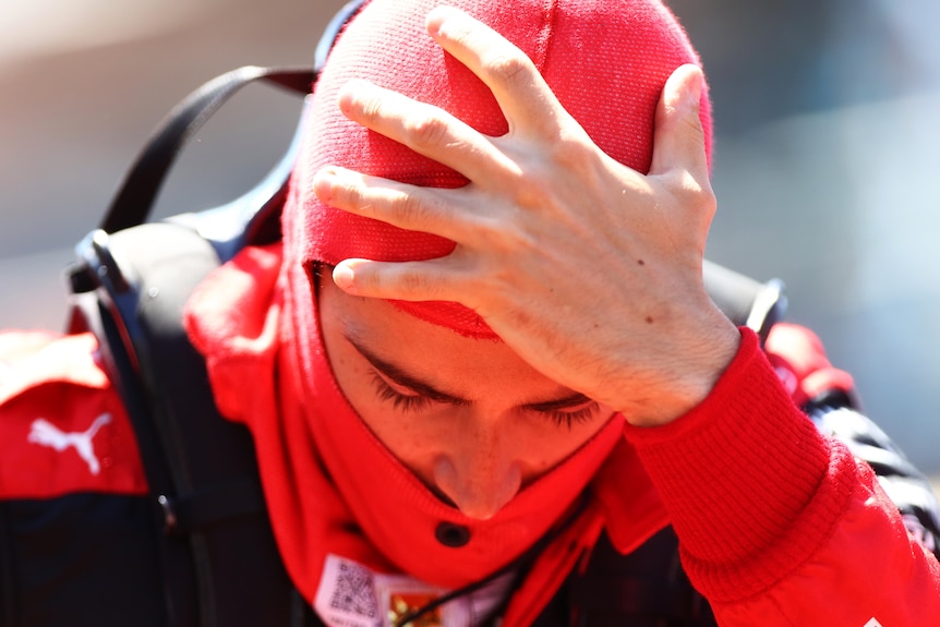 Race driver wearing red hold his head. 