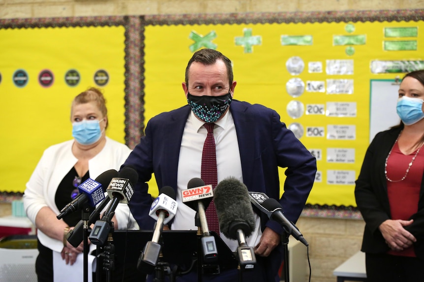 A man stands behind a group of microphones in front of a yellow wall